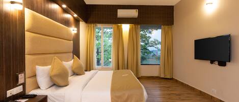 A modern hotel room with a large bed, a flat-screen TV, and a view of trees through the window.