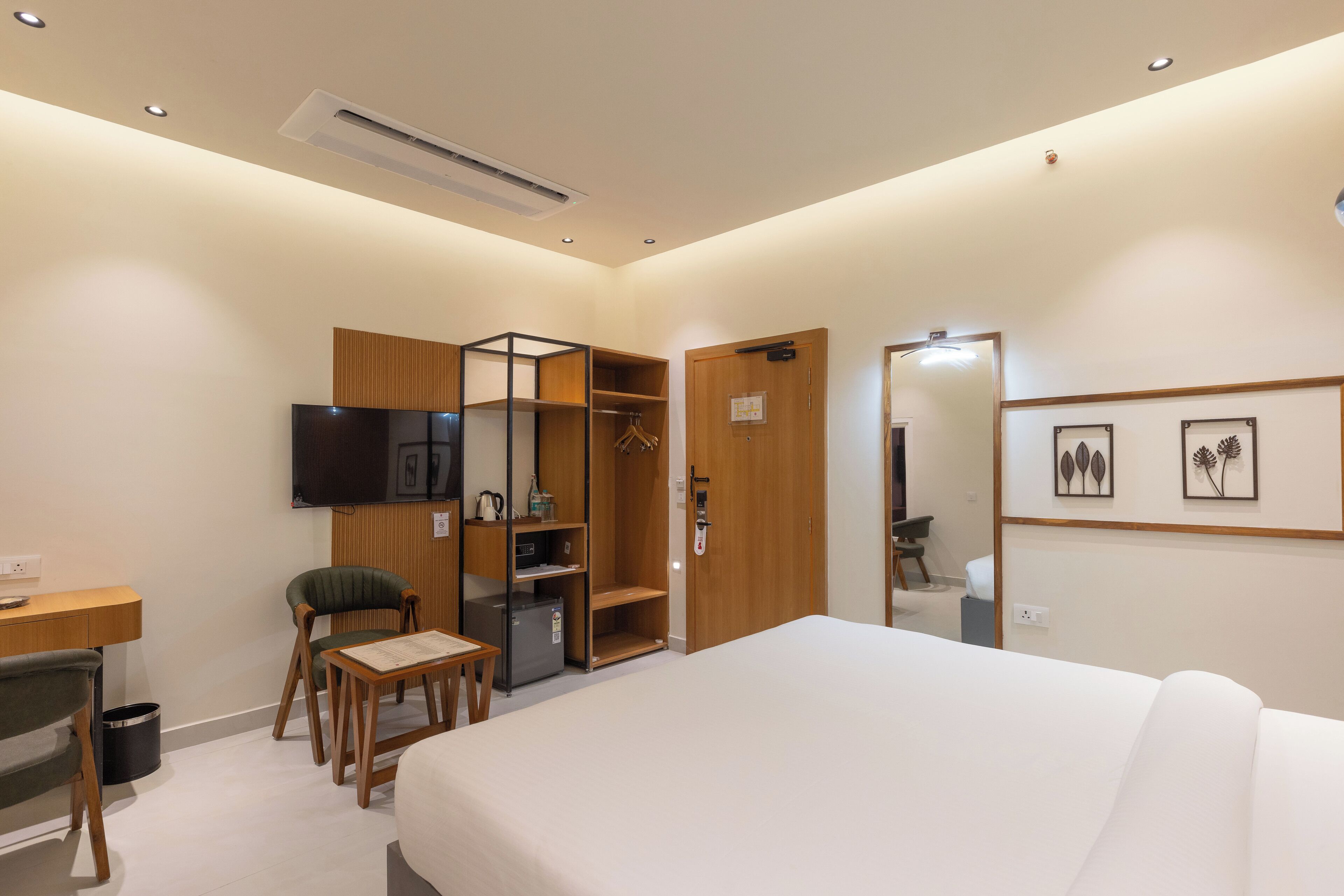 A hotel room with a bed, a desk with a chair, a wardrobe, a television, and framed pictures on the wall.