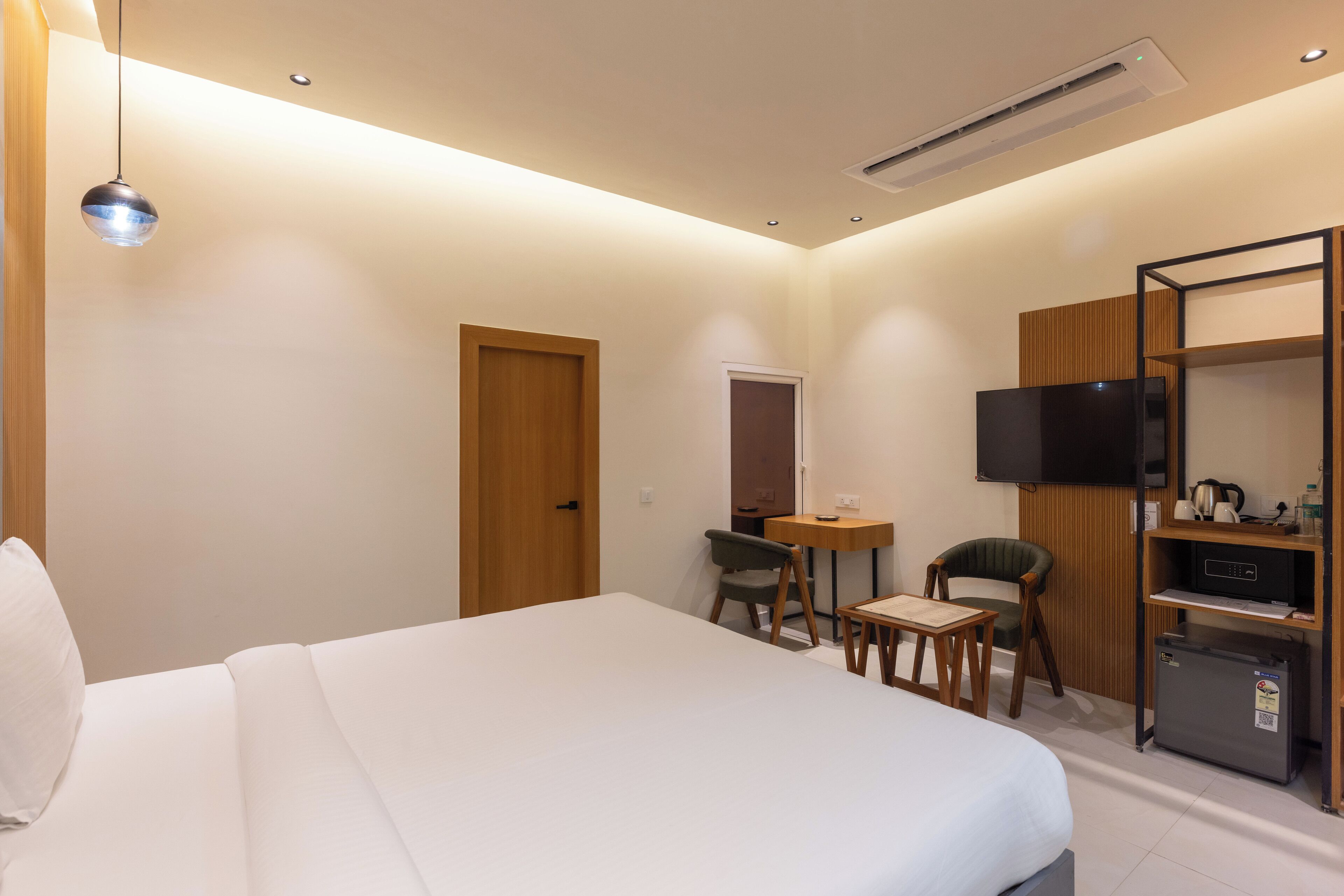 Ein modernes Hotelzimmer mit einem großen Bett, einem Schreibtisch mit Stuhl, einem Fernseher und einer kleinen Küchenzeile.