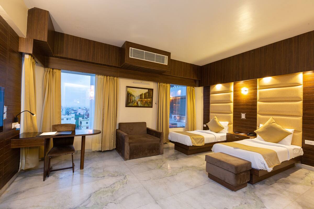 A hotel room with a desk, two beds, a chair, and a view of the city.