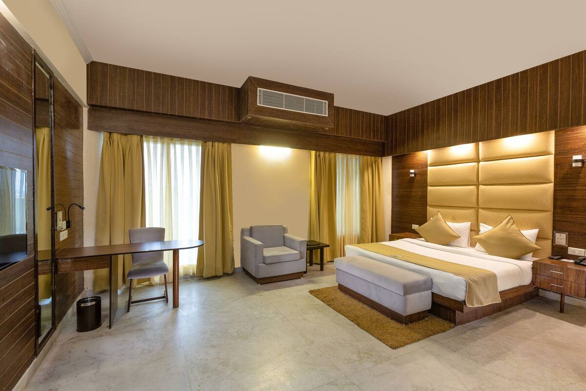 A modern hotel room with a large bed, a desk, a chair, and a small table.