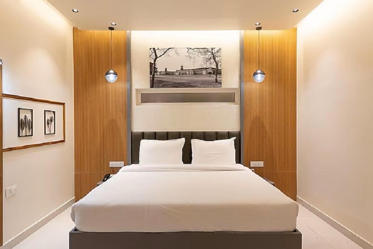 Una habitación de hotel moderna con una cama grande, paneles de madera, dos lámparas empotradas en la pared y un cuadro enmarcadosobre la cama.