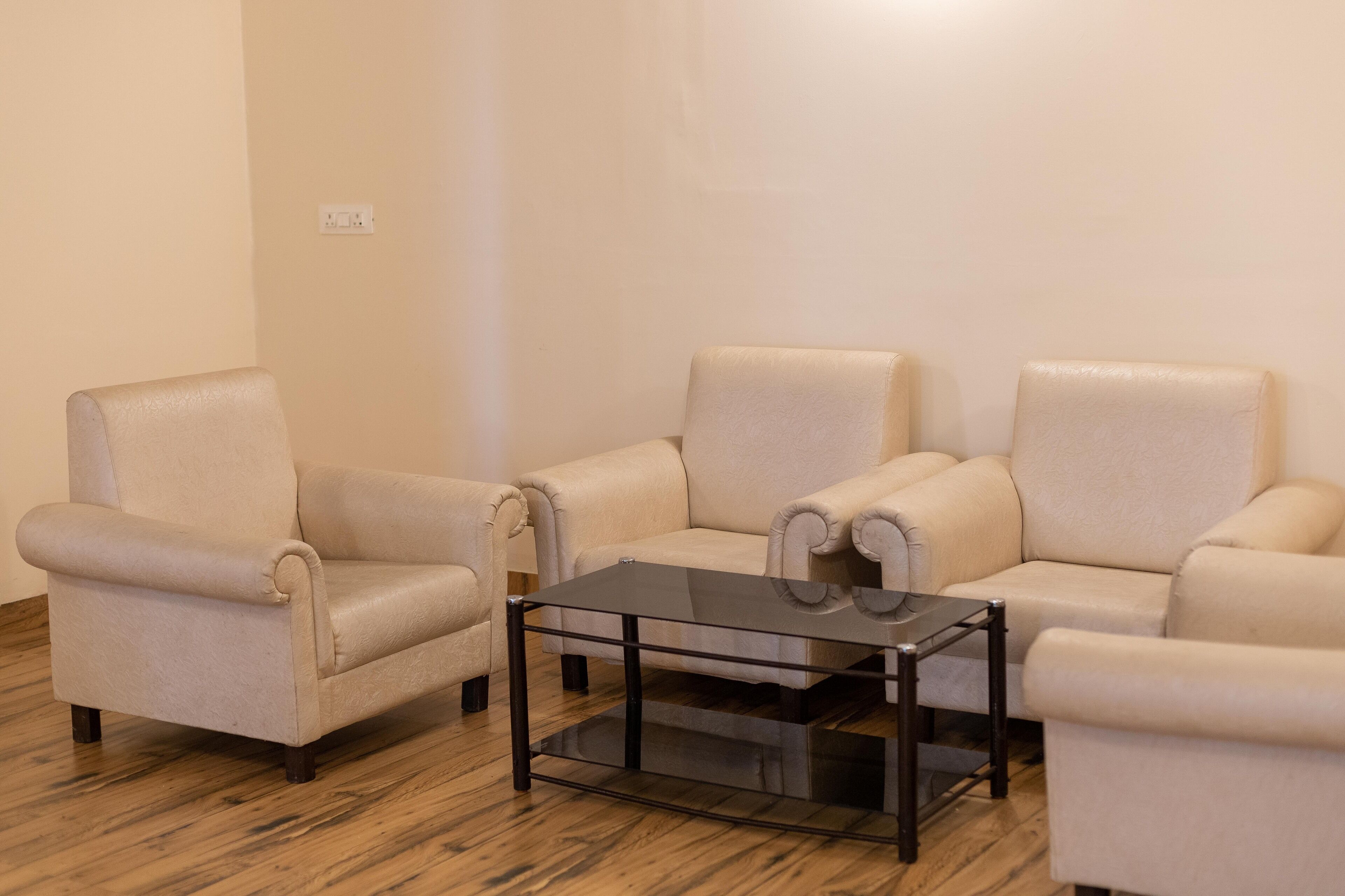 A room with three beige armchairs and a glass-top coffee table.