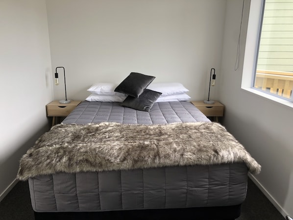Un dormitorio con cama, dos mesitas de noche y una ventana.