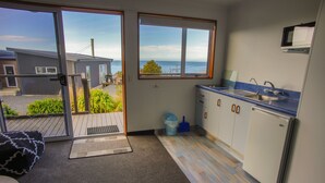 A compact kitchen with a view of the sea, a small trash bin, and a door leading to an outdoor area. - The Kaka Point Motels (Kaka Point)
