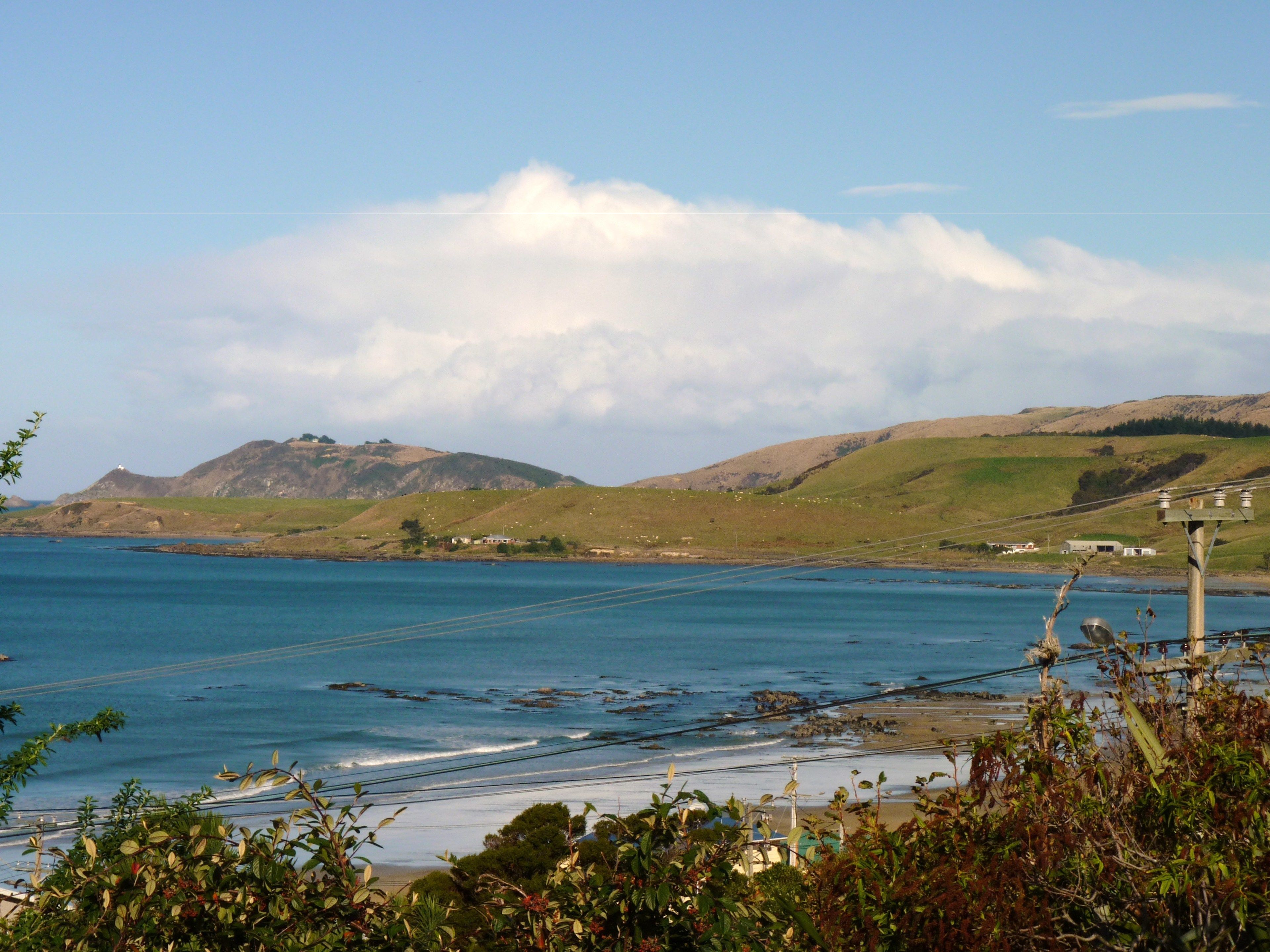 A coastal landscape with a view of the sea, hills, and a power line structure.