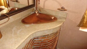 Une salle de bain avec un lavabo en cuivre, un miroir et un porte-serviettes.