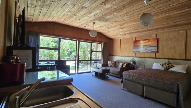 A room with a bed, a desk, and a large window. - The Rocks Chalets (Takaka)