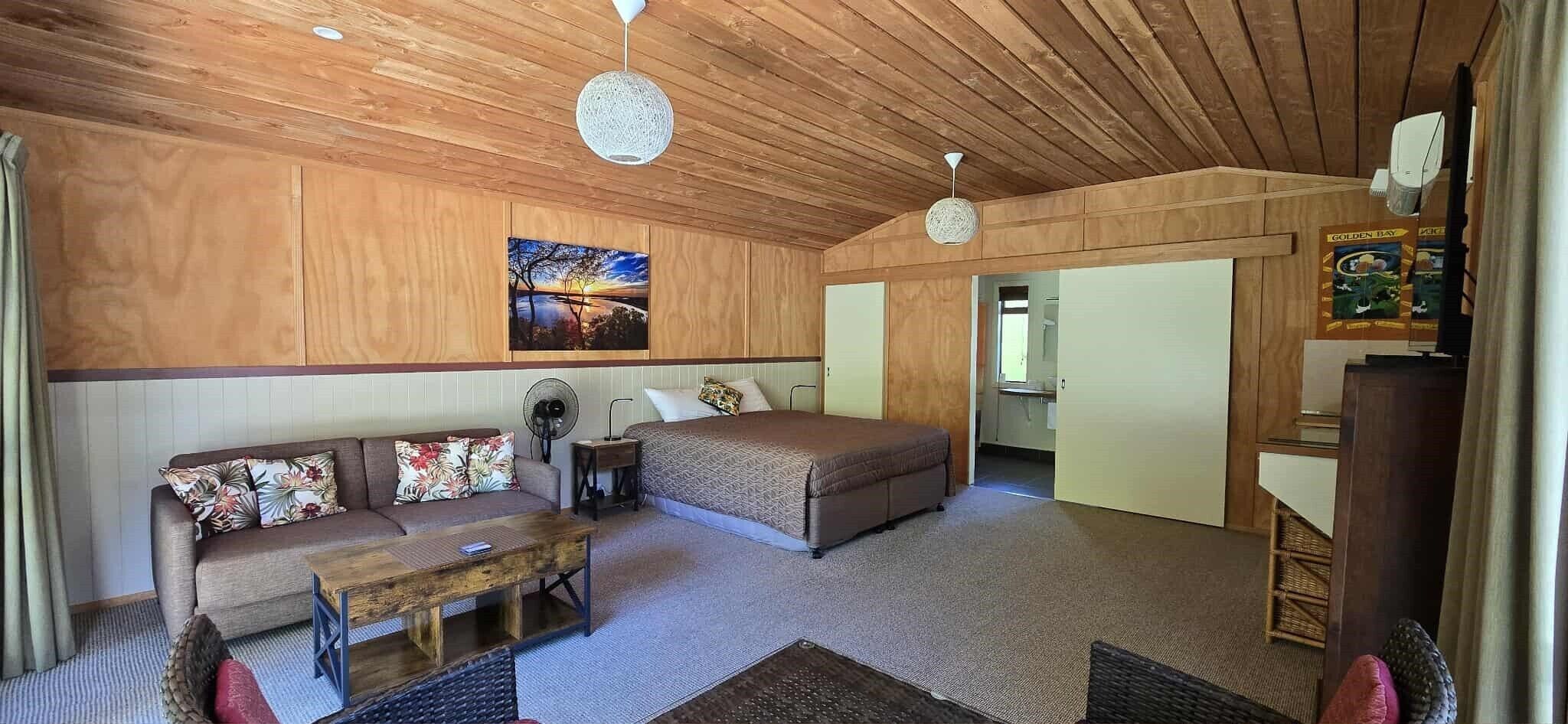 A cozy room with a sofa, a bed, a wooden ceiling, and a painting on the wall.