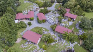 An aerial view of a resort with multiple buildings, a central paved area, and surrounding greenery. - The Rocks Chalets (Takaka)