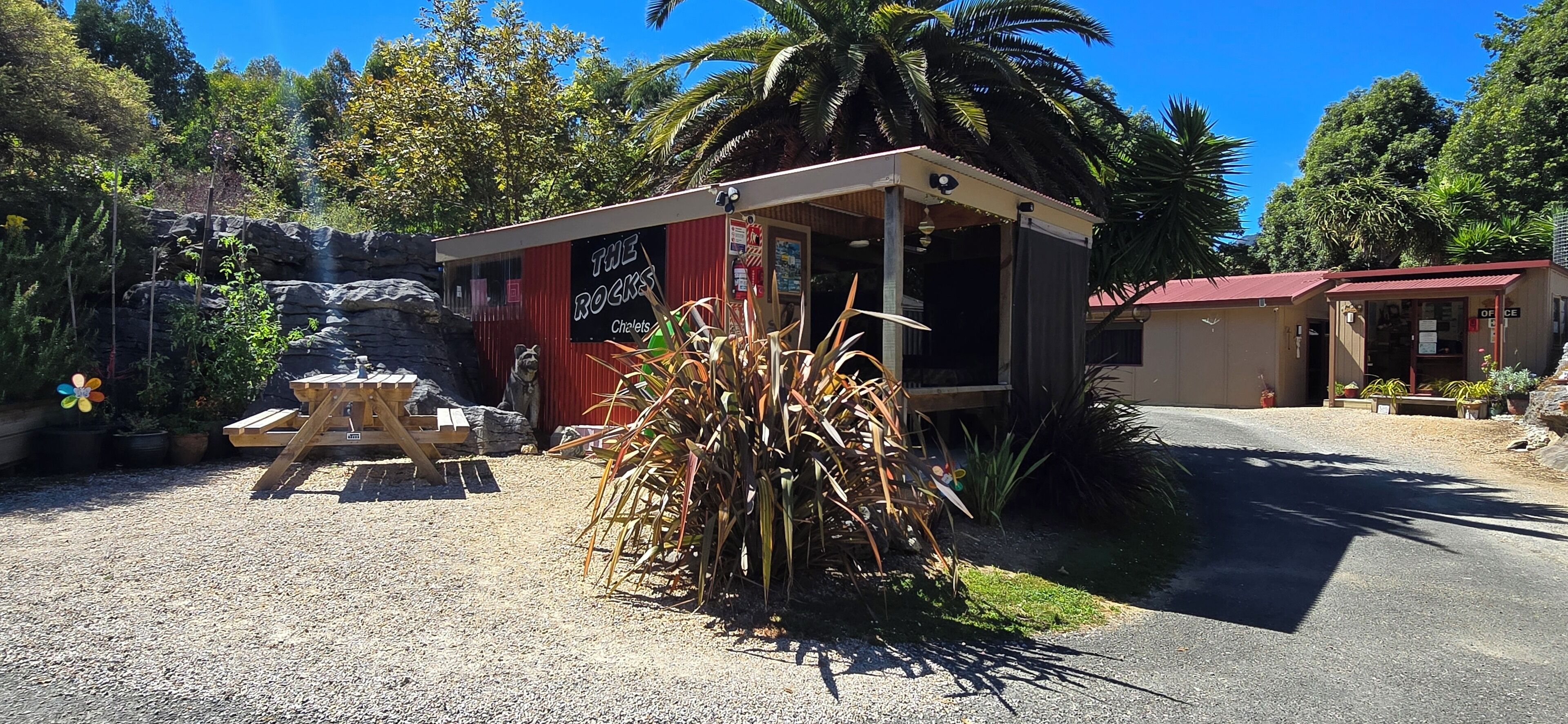 A small building with a red roof, a wooden picnic table, and a pile of dried plants in front.