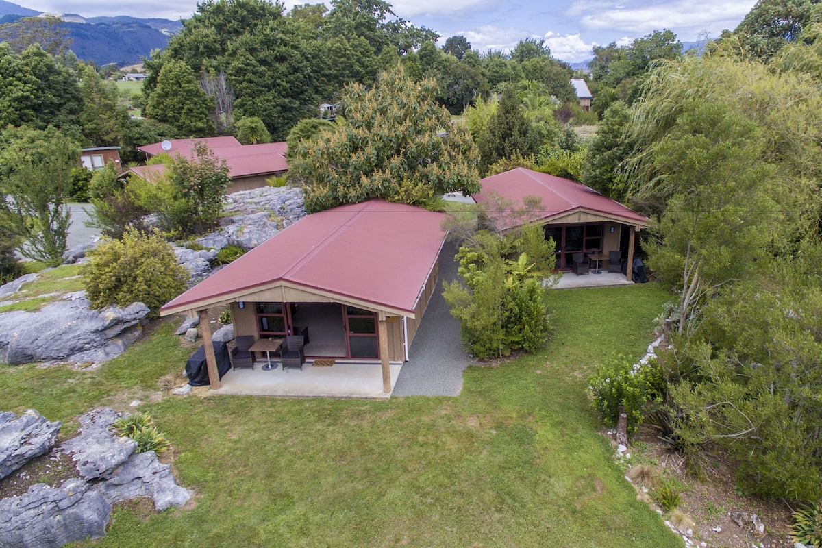 A two-story house with a red roof, a covered patio with outdoor furniture, and a view of surrounding trees and hills.