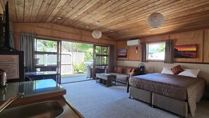 A room with a bed, a sofa, a small table, and a window. There is a sign on the table and a fan near the sofa. - The Rocks Chalets (Takaka)