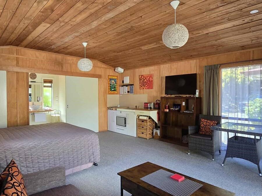Une pièce confortable comprenant un lit, une petite kitchenette, un coin repas avec des meubles en osier et une grande fenêtre donnant sur un paysage agréable.