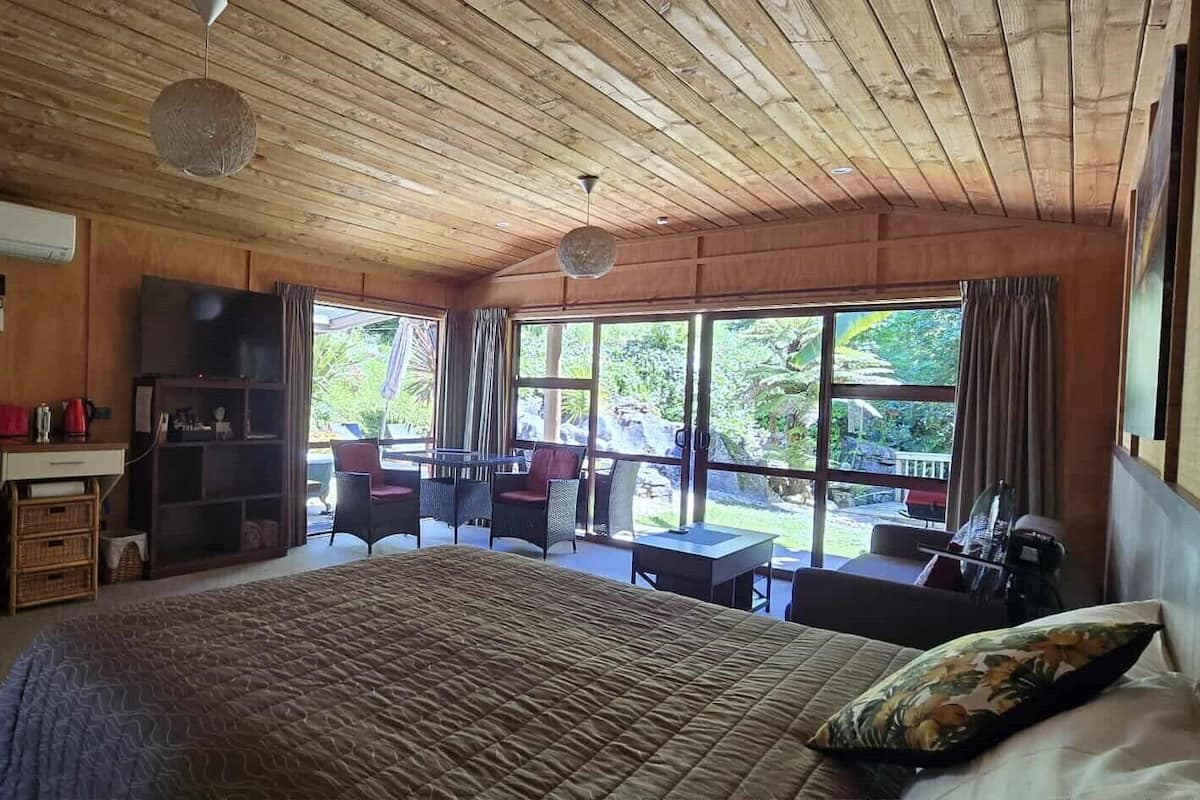 A bedroom with a large bed, a small kitchenette, and a dining area with a view of the outdoors.
