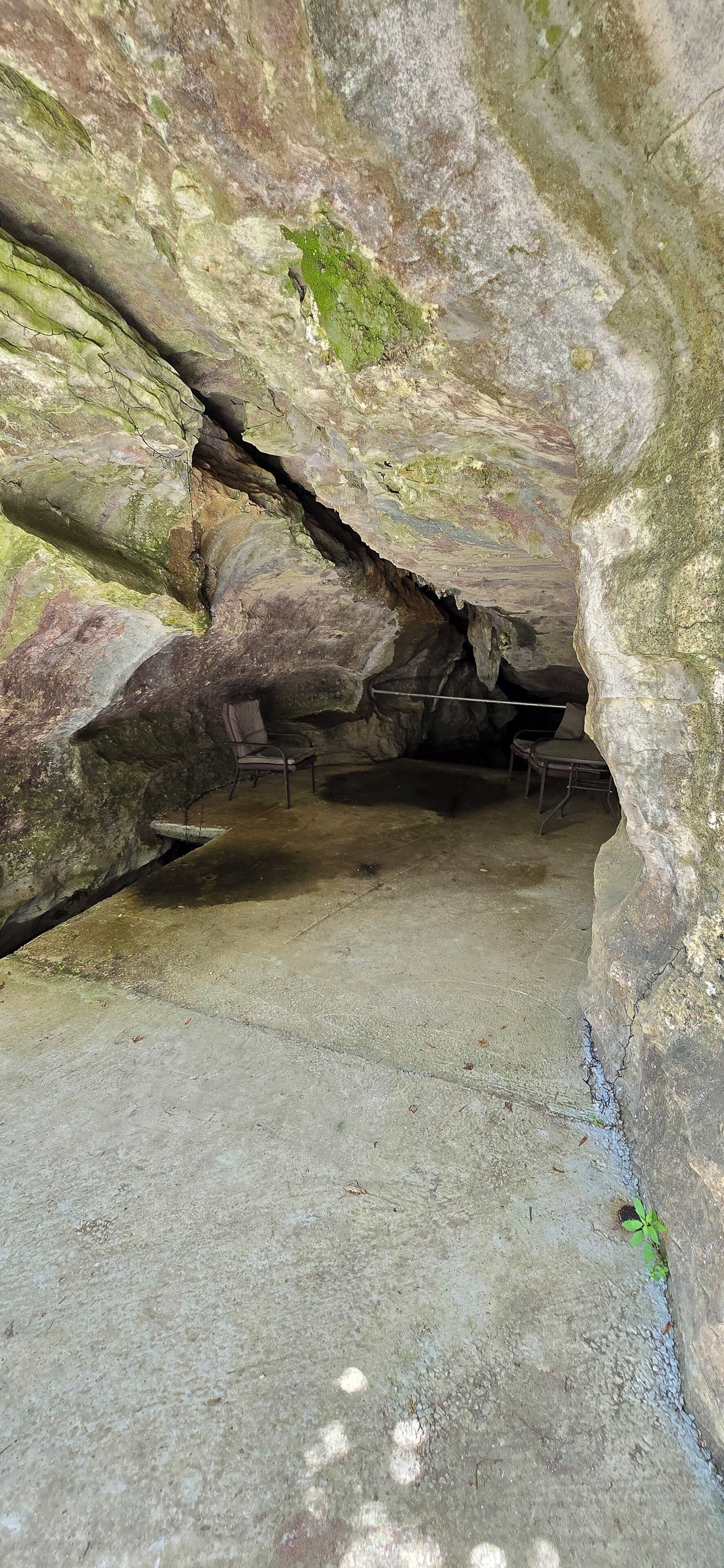 A cave interior with a concrete floor, rock formations, and metal chairs.