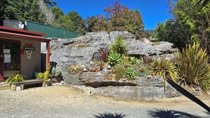 A building with an office sign, a gravel driveway, and various potted plants. - The Rocks Chalets (Takaka)