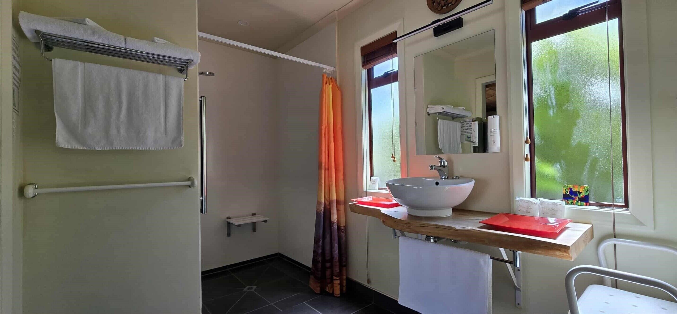 Un baño con un lavabo blanco, un espejo, toallero, cortina de ducha y ventana con vistas.