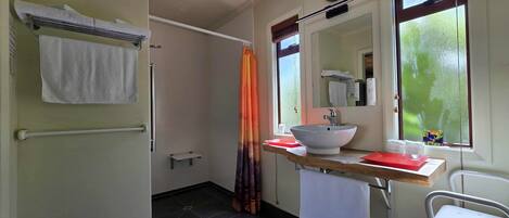 Un baño con un lavabo blanco, un espejo, toallero, cortina de ducha y ventana con vistas.