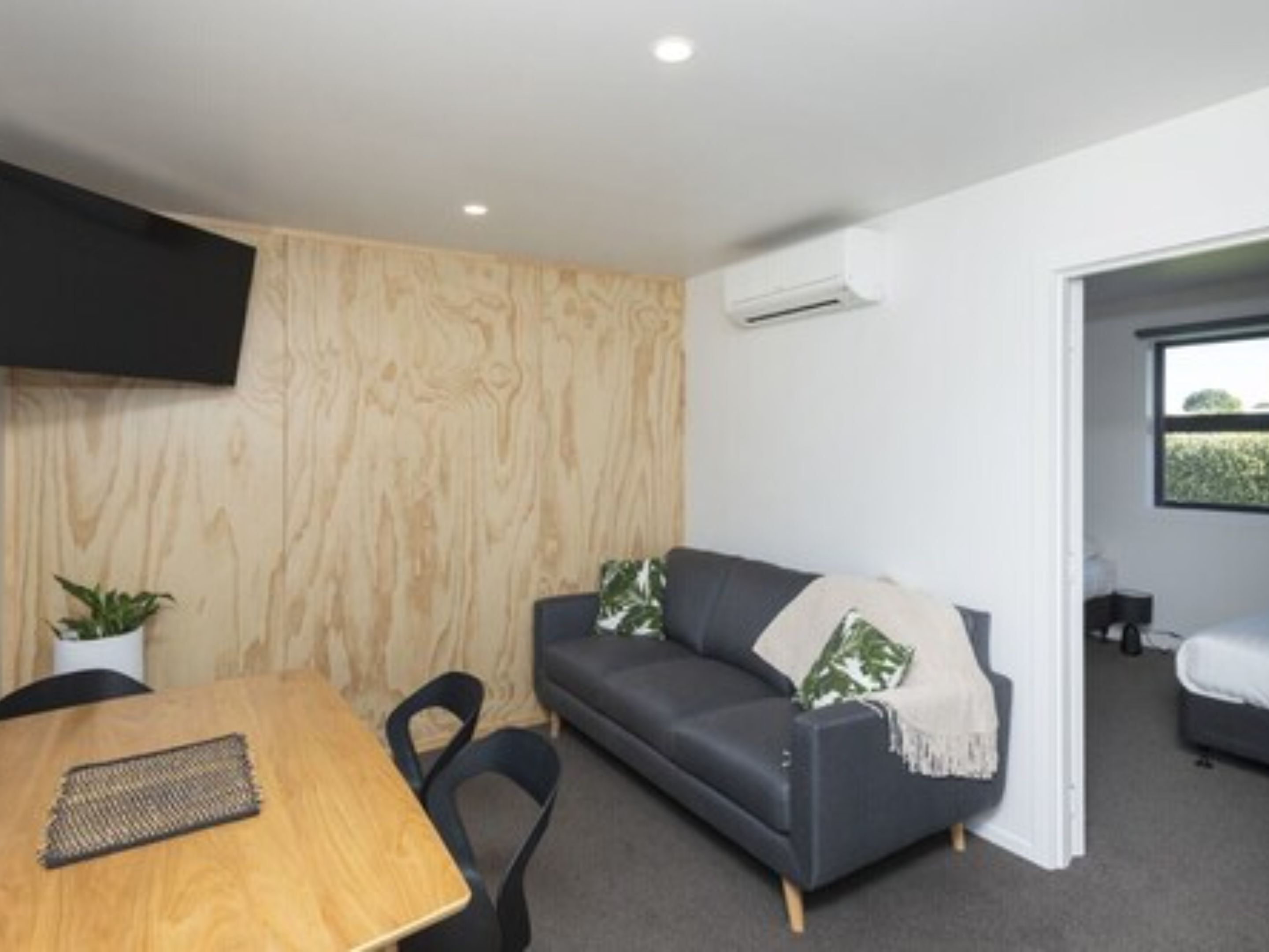 Une pièce moderne avec un mur en bois, un canapé gris agrémenté d’une couverture, une petite table et un téléviseur fixé au mur.