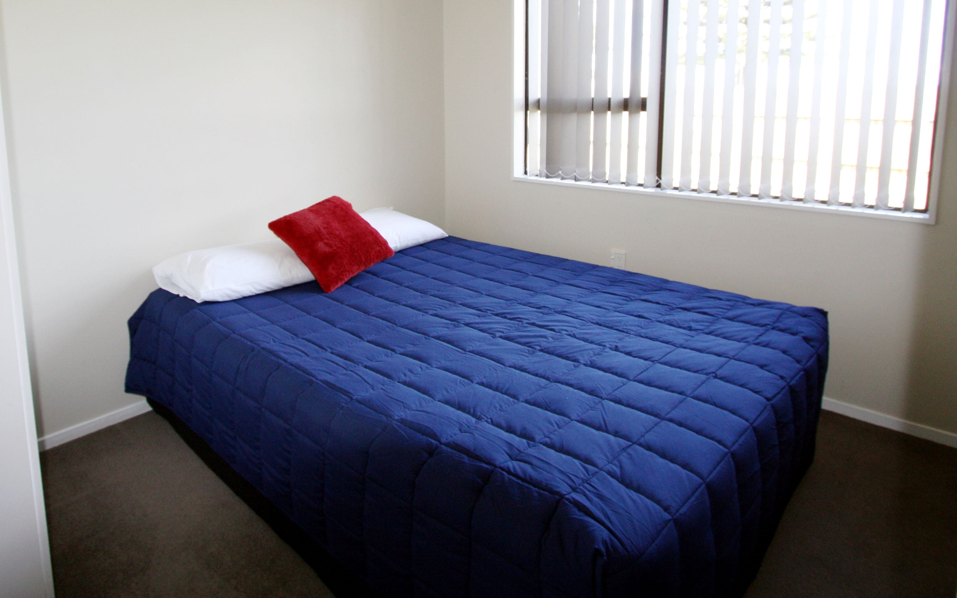 Quarto com colcha azul, almofadas brancas e almofada decorativa vermelha.