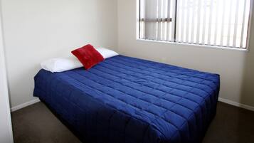 Quarto com colcha azul, almofadas brancas e almofada decorativa vermelha.