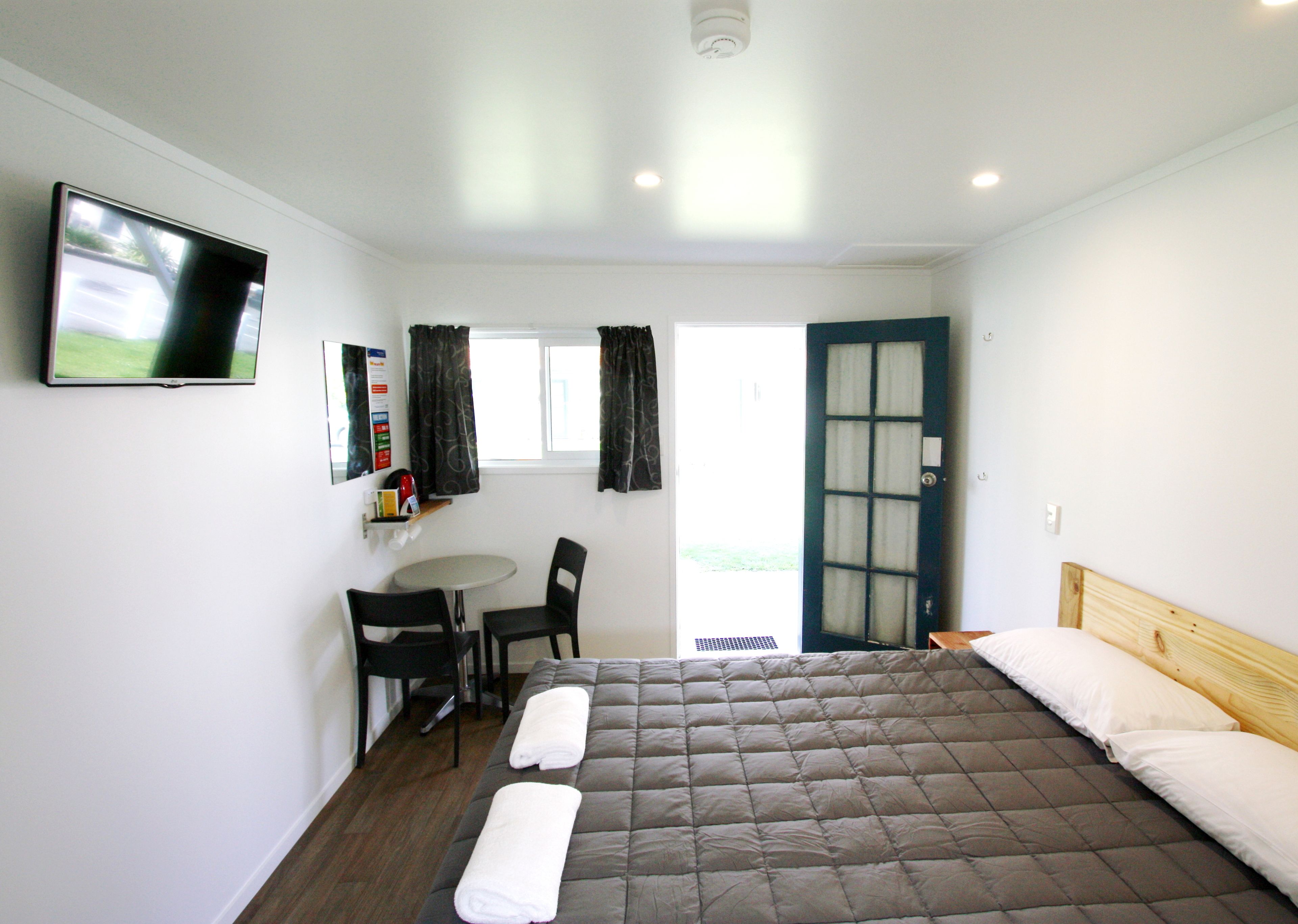 A hotel room with a bed, a TV, a small table with chairs, and a window with curtains.