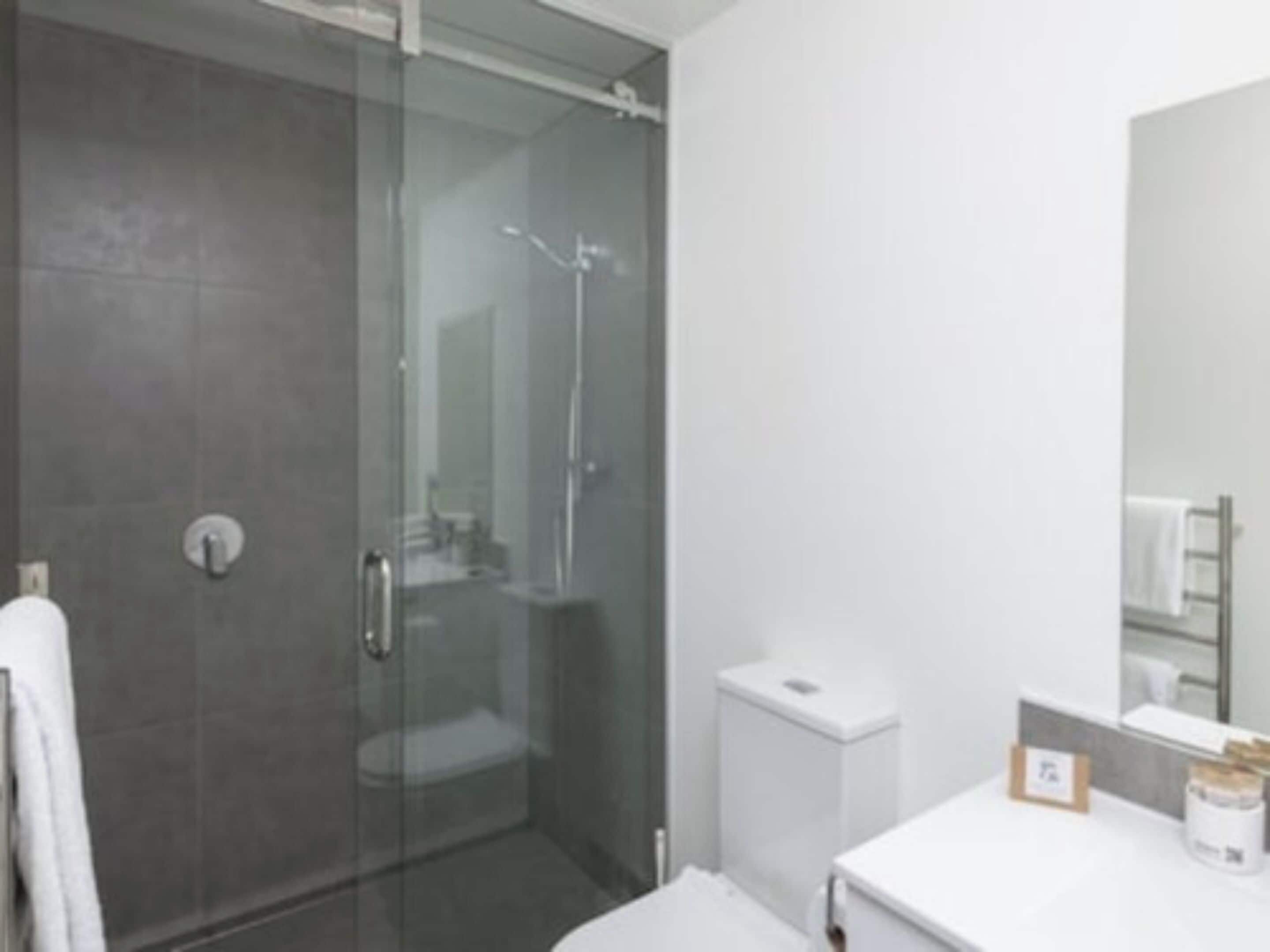 A modern bathroom with a glass shower enclosure, a white sink, and a mirror above the counter.