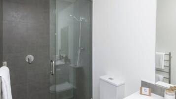 A modern bathroom with a glass shower enclosure, a white sink, and a mirror above the counter.