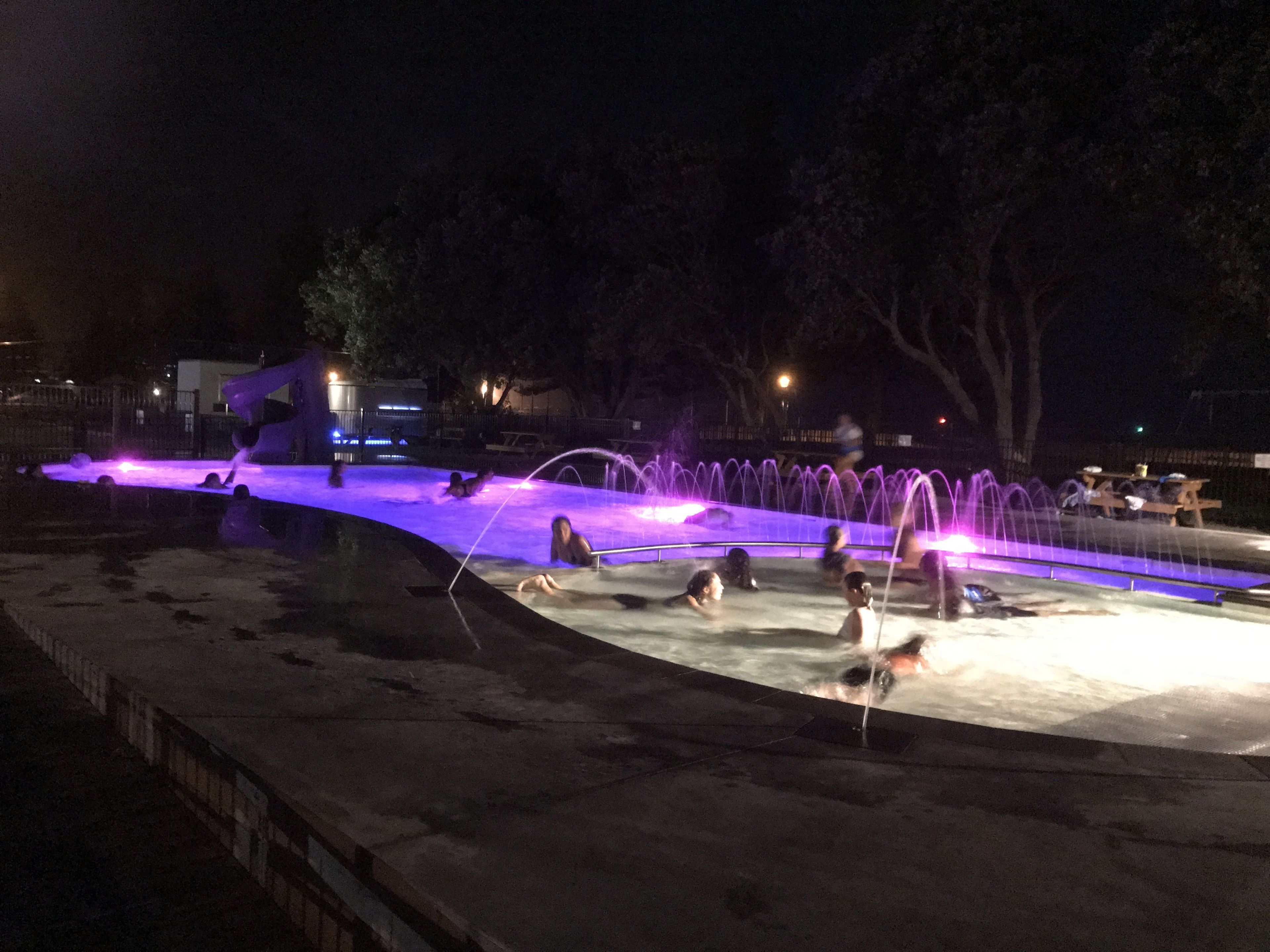 Een zwembad bij nacht met verlichte waterpartijen en een betonnen terras.