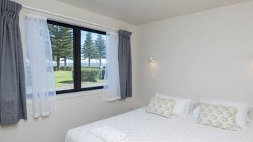 Un dormitorio con una cama grande, una ventana con cortinas, una lámpara fijada a la pared y vistas al verdor exterior.