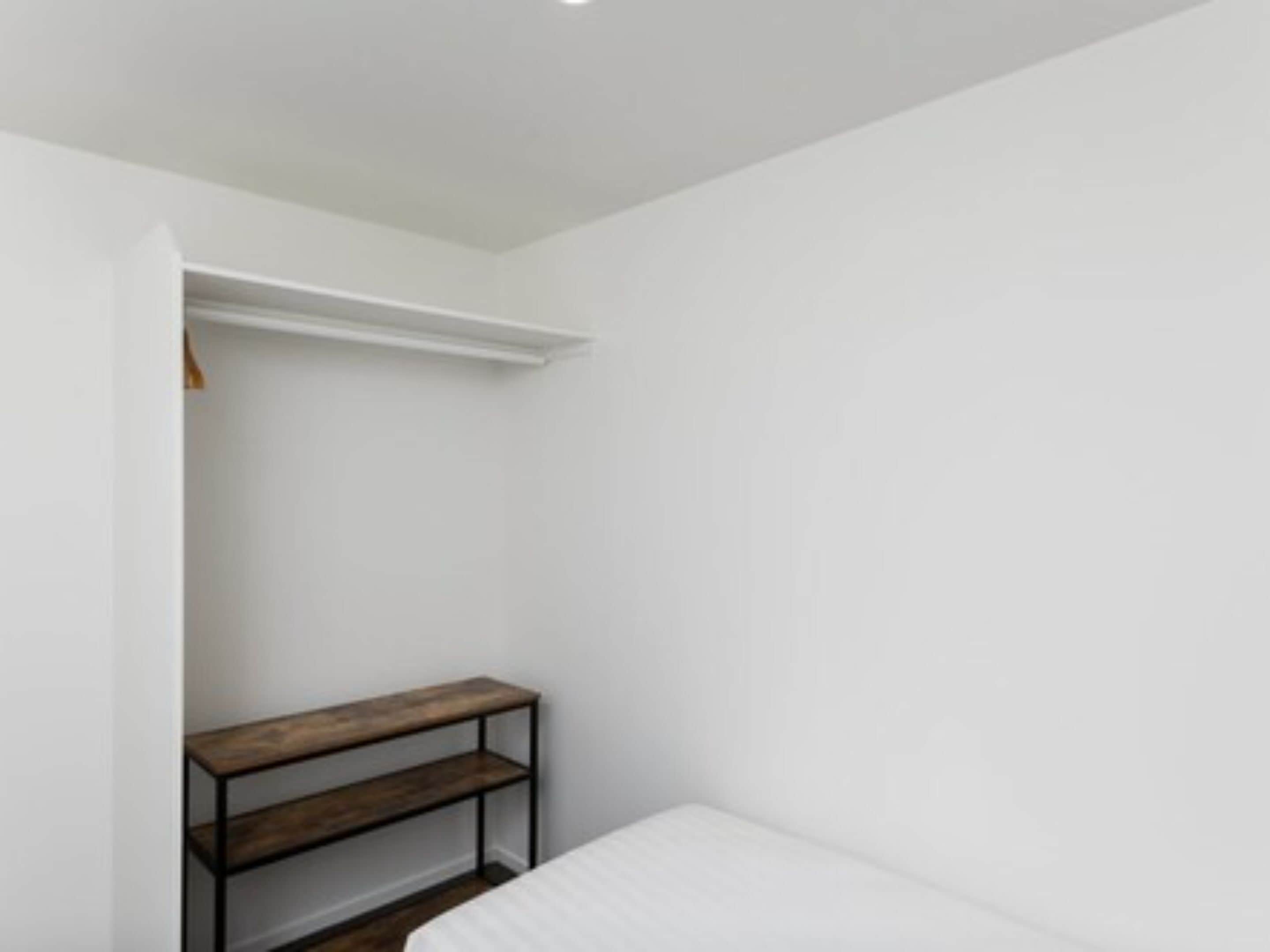 Une chambre avec un lit simple, un banc en bois et un mur blanc.