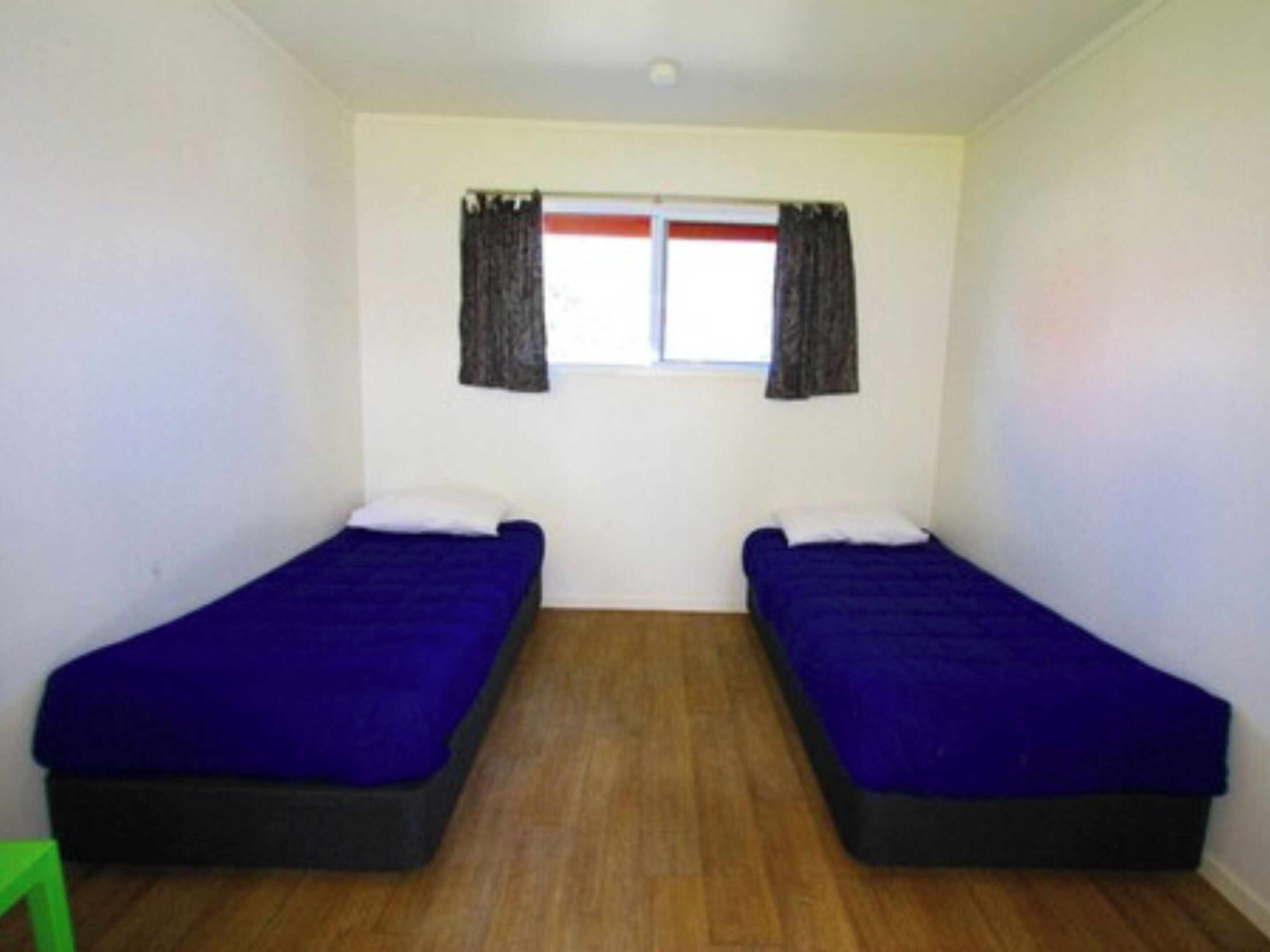 Une chambre avec deux lits simples, une fenêtre avec des rideaux et un plancher en bois.