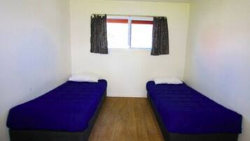 Une chambre avec deux lits simples, une fenêtre avec des rideaux et un plancher en bois.