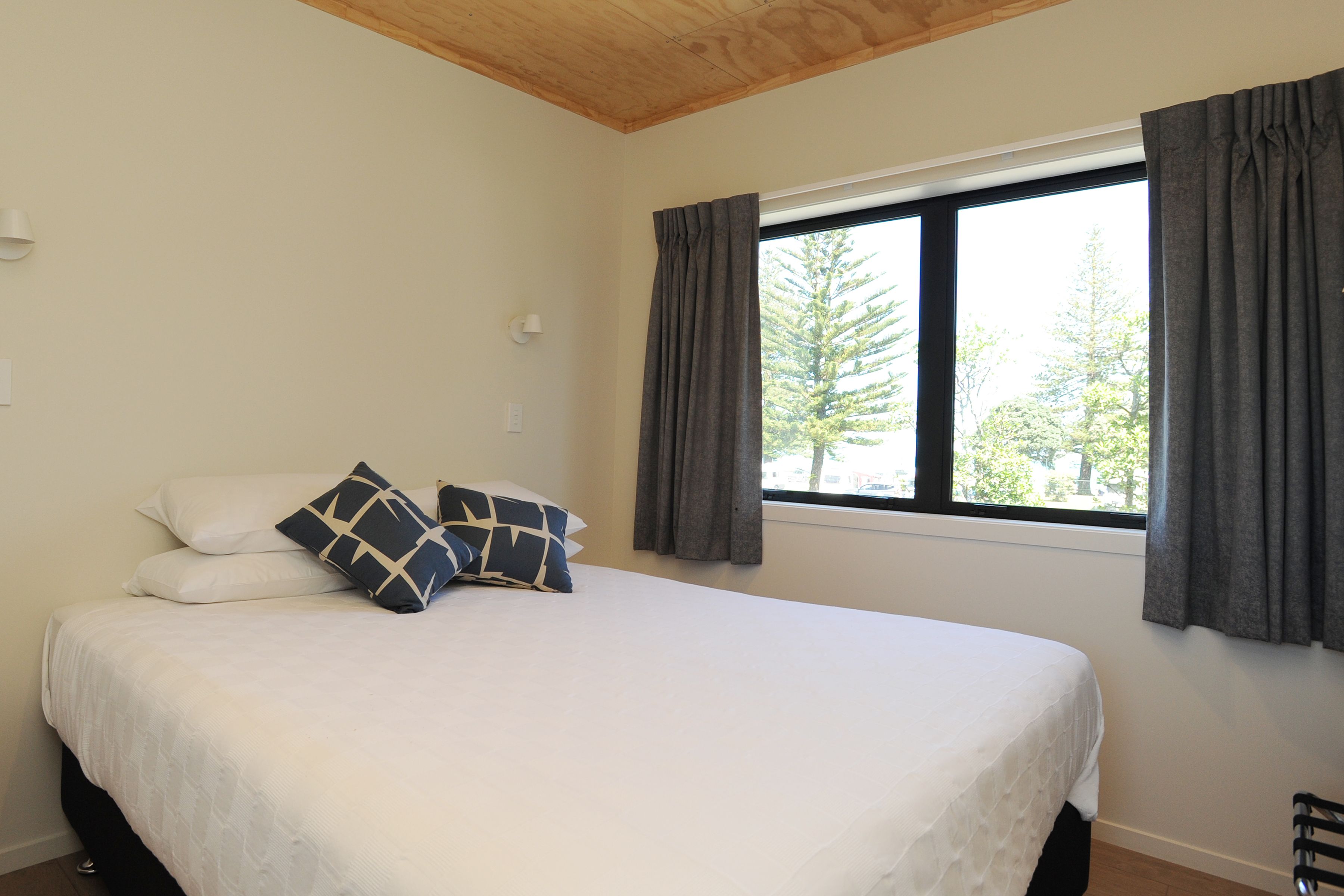 Ein Schlafzimmer mit einem großen Bett, zwei Kissen, einem Fenster mit Vorhängen und einer Holzbalkendecke.