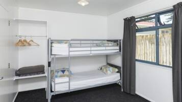 A bunk bed room with a window, a shelf with hangers, and a small desk.