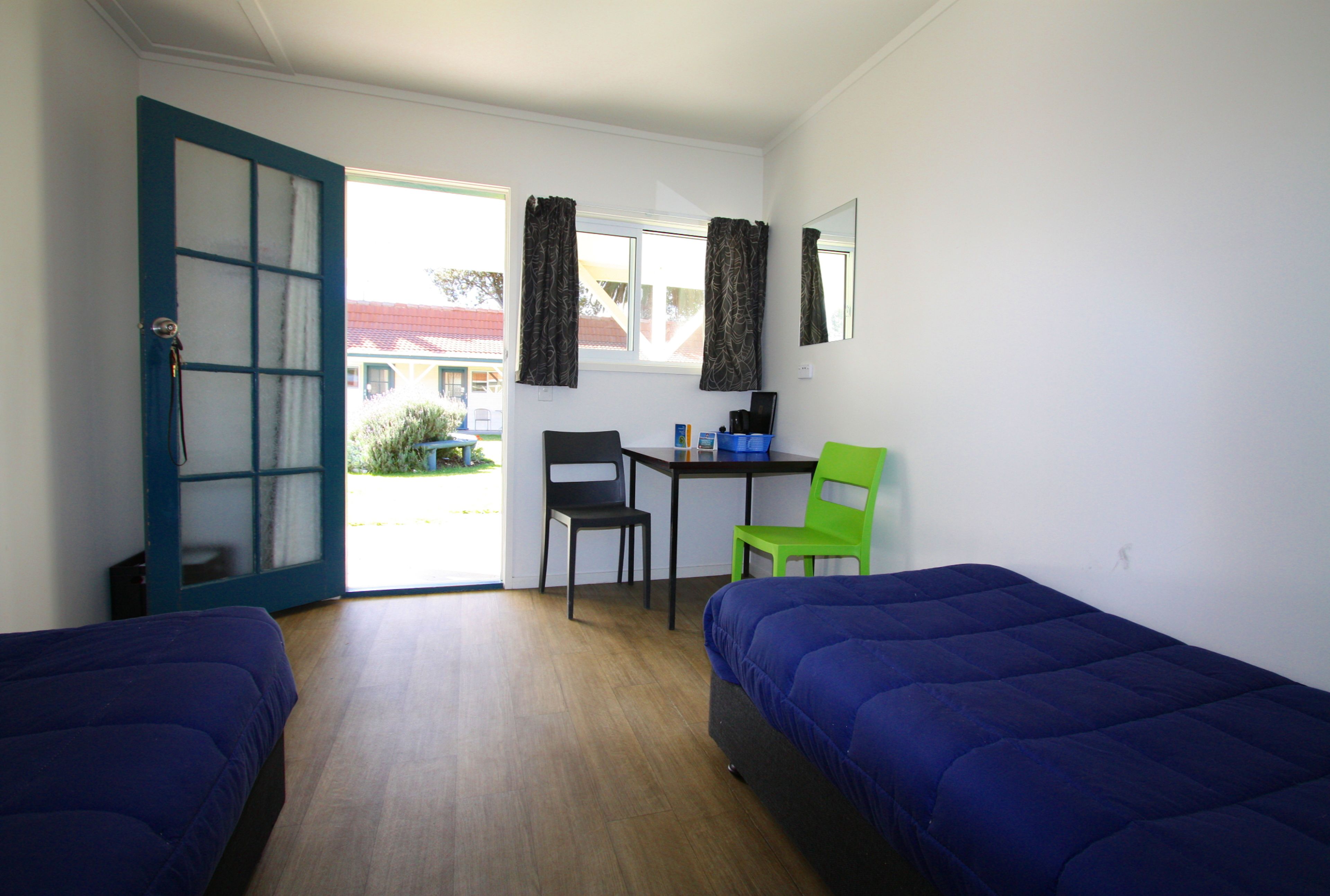 A room with two beds, a desk, two chairs, and a window with curtains.