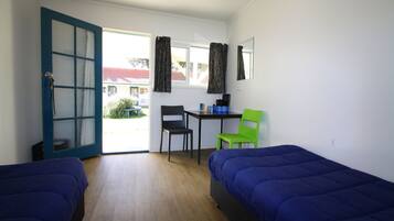 A room with two beds, a desk, two chairs, and a window with curtains.