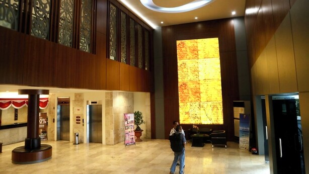 Een ruime lobby met een grote verlichte muur, een receptiebalie en een trap naar een verdieping erboven.