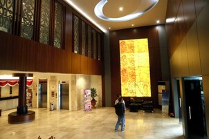 Um hall amplo com uma grande parede iluminada, um balcão de recepção e uma escadaria para um andar superior.