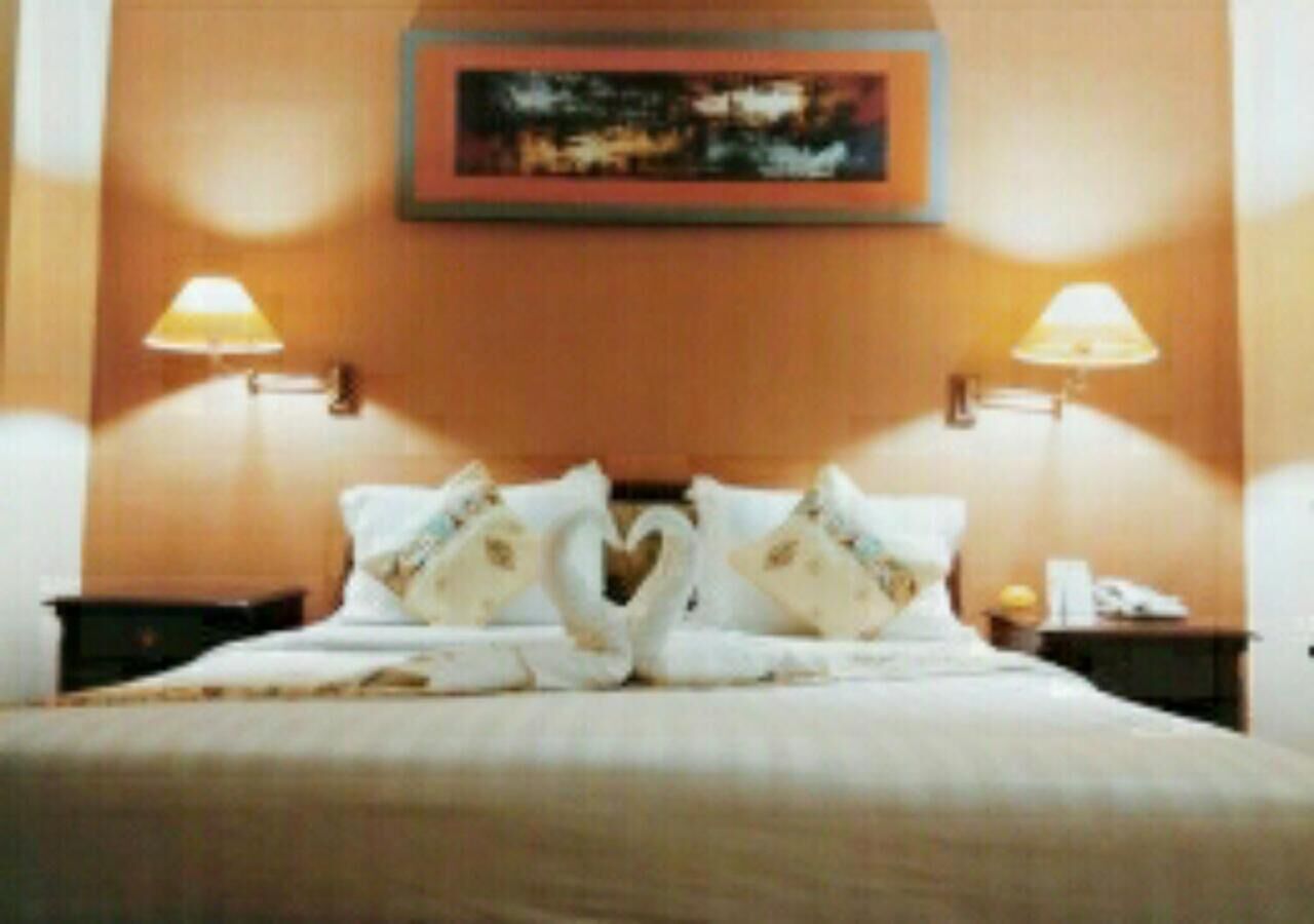 Une chambre d’hôtel avec un lit, deux lampes de chevet, un tableau au mur et un élément décoratif en forme de cœur sur les oreillers.