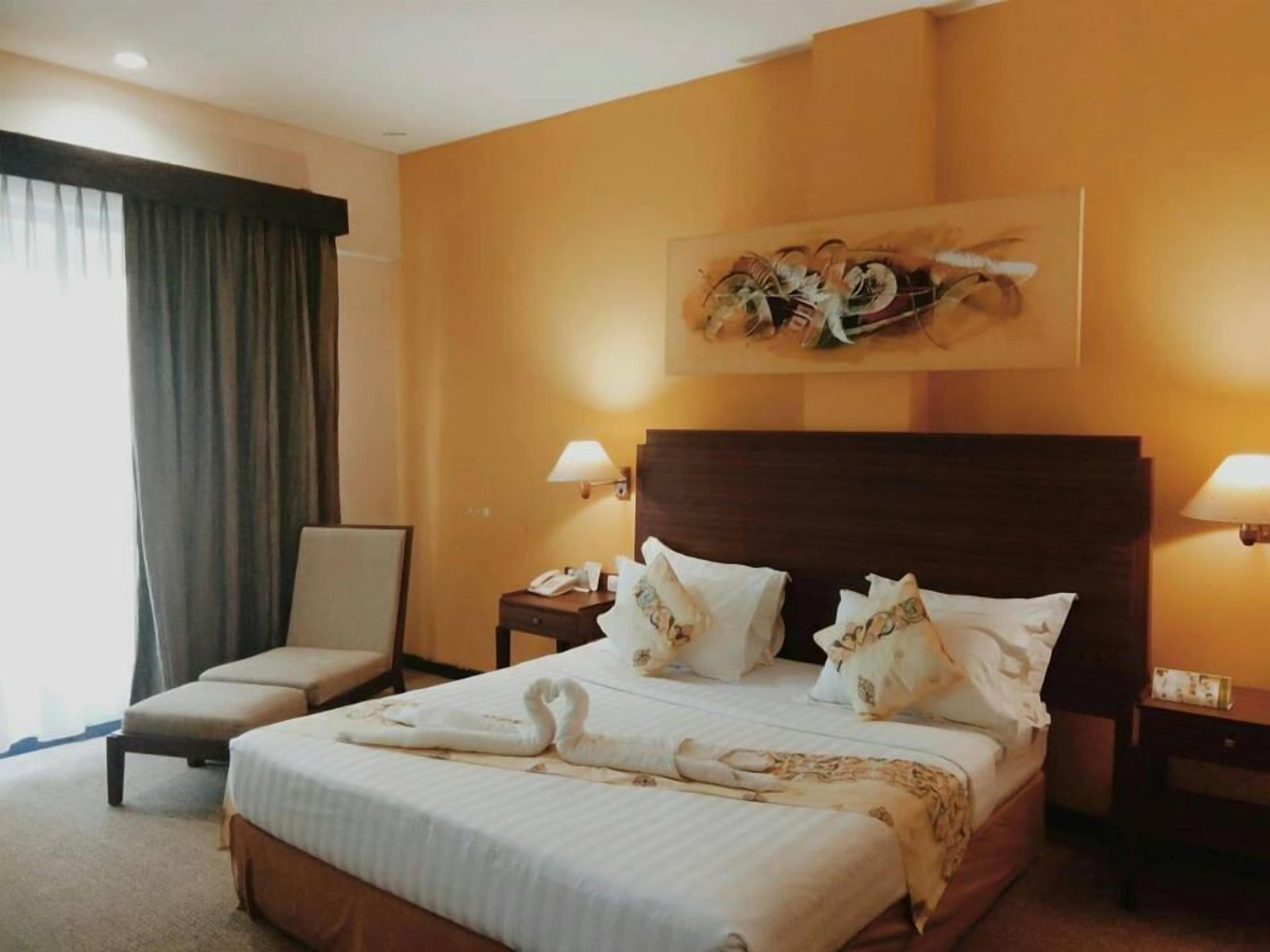 Habitación de hotel con una cama grande, dos mesitas de noche, una silla y un cuadro en la pared.