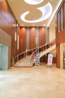 Um hall de hotel moderno com escadaria de mármore, painéis de madeira e design de teto iluminado.