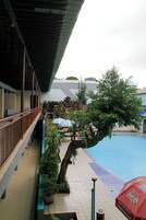Área de piscina com árvore, guarda-sóis e um edifício com varanda.