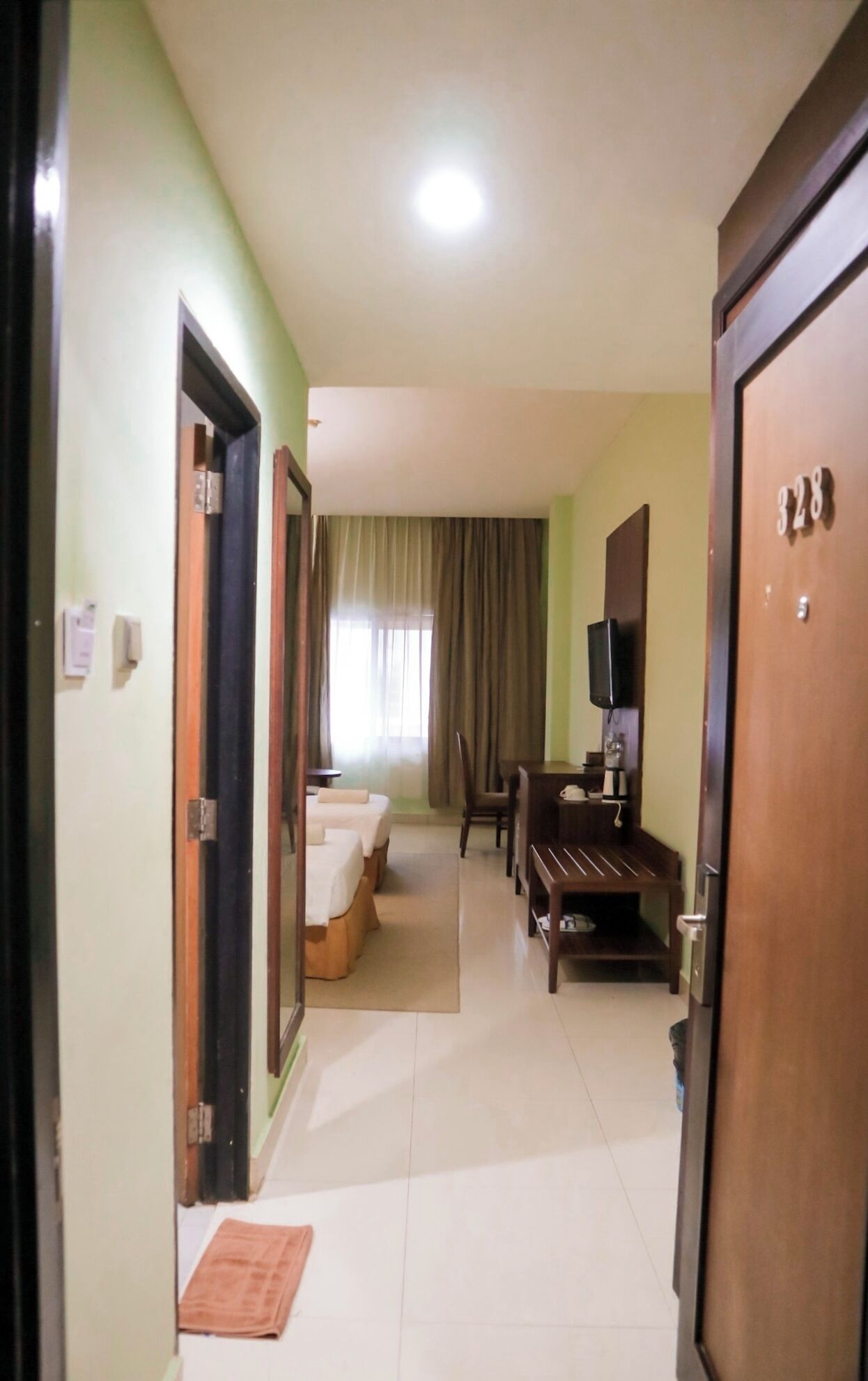 Une chambre d’hôtel avec un lit, un bureau, une chaise, une télévision et une porte portant le numéro 328.