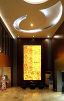 Um lobby moderno com uma grande parede iluminada, área de estar e balcão de recepção.