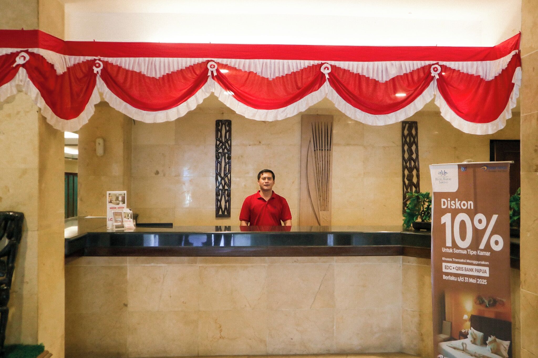 A reception desk with a man standing behind it, red and white drapes above, and a sign advertising a 10% discount.
