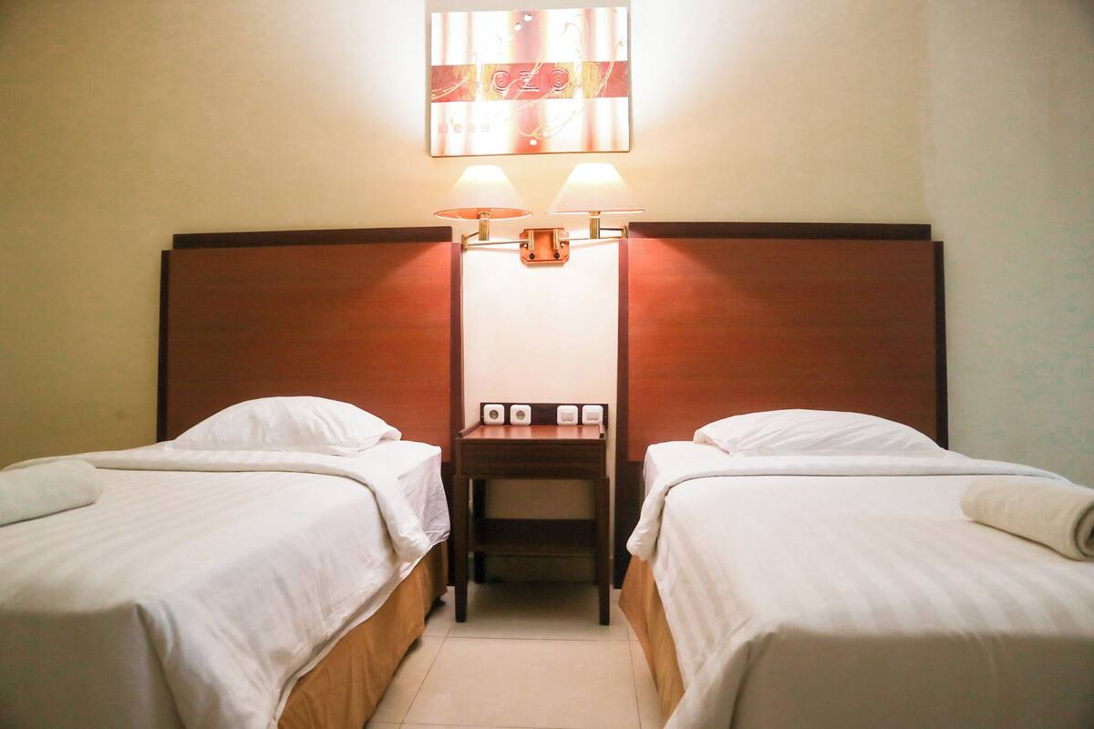 Hotellihuone, jossa on kaksi erillistä sänkyä, yöpöytä lampun kanssa ja seinään kiinnitetty valaisin.