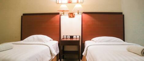 A hotel room with two single beds, a nightstand with a lamp, and a wall-mounted light fixture.