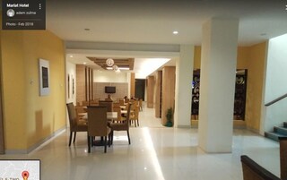 Um hall de hotel moderno com uma ampla área de refeições, uma TV de tela plana na parede e uma escada que leva a outro andar.